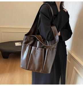 Detail of a large dark brown faux leather shoulder bag with functional outer pockets