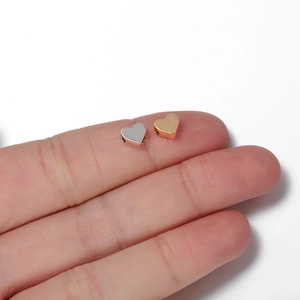 Gold and silver heart-shaped spacer beads for jewelry DIY shown on a fingertip