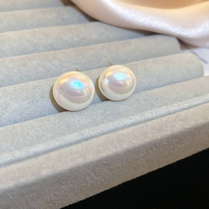 Macro detail of French bow pearl stud earrings with golden pins on grey velvet tray