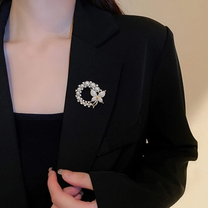 Détail d'une broche fleur papillon dorée avec perles sur le revers d'un blazer noir