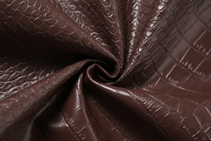 Detailaufnahme von dunkelbraunem Kunstleder mit Krokodilprägung und glänzendem Finish