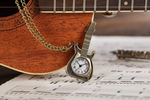 Close-up of guitar-shaped bronze pocket watch with quartz dial on a musical sheet