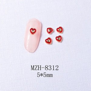 Macro detail of red heart nail art charm with gold beaded edges on pink manicure