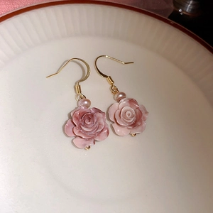 Dettaglio di orecchini a rosa rosa con ganci dorati e delicati accenti di perle