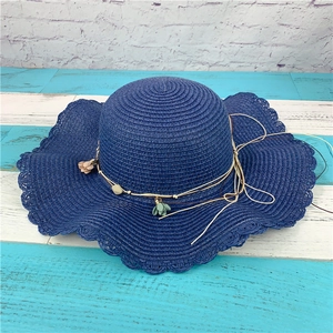 Detail of dark blue straw sun hat with wavy brim, decorative cord and floral bead charm