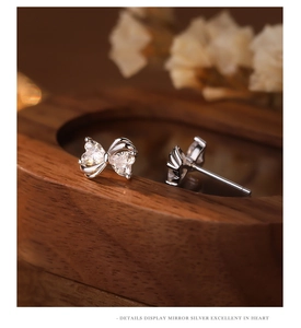 Macro shot of silver bow earrings with heart zircons on wooden stand