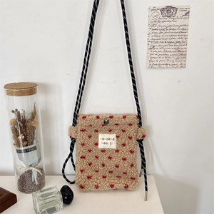 Detailed shot of beige plush crossbody bag featuring red hearts and woven rope strap