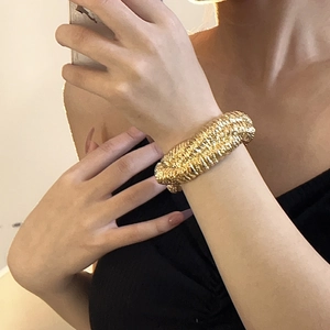 Close-up of a wide gold cuff bracelet featuring intricate lava-like woven metal textures