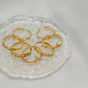 Stack of gold stainless steel open rings with engraved letters on a textured tray