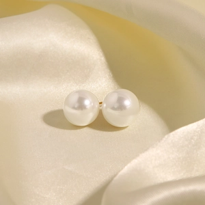 Detailed close-up of cream-white pearl earrings on elegant beige silk fabric texture