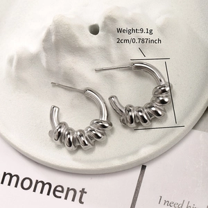 Macro view of silver-tone twisted C-shape earrings on white stone tray with dimensions