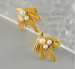 Close-up of gold swallow wing earrings with white pearls on a textured background