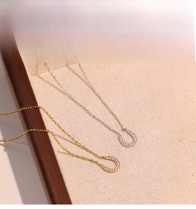Detail of horseshoe pendants in gold and silver with zircon pave on linen surface