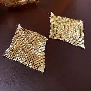 Golden geometric mesh earrings with polished triangular accents on dark leather