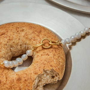 Close-up of 18k gold plated pearl bracelet with twisted clasp on a metallic plate