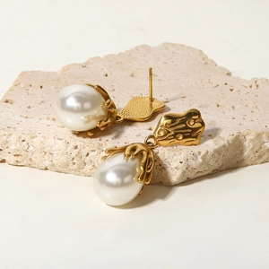 Macro detail of round white pearl earrings with golden textured coral-like metal finish
