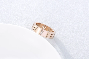 Detail of rose gold cutout Roman numeral ring leaning on white ceramic plate