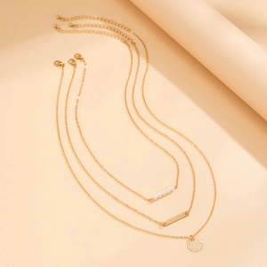 Detail of triple-layer gold necklace with faux pearls and hammered metal pendants