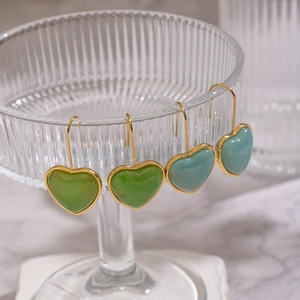Gros plan de boucles d'oreilles cœur en résine verte avec bord doré sur un verre élégant