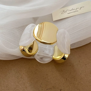 Détail de bracelet gourmette dorée avec maillon irrégulier en résine acrylique blanche
