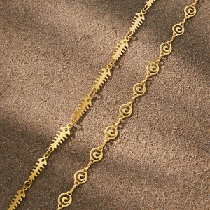 Detailed shot of golden fishbone and spiral wave necklaces on beach sand texture
