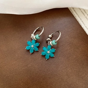 Detail of silver hoop earrings with green flower pendant and small beads on kraft paper