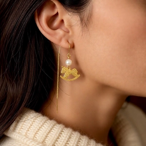Detailed view of elegant gold rocking horse earrings with pearls worn by a model