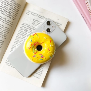 Close-up of a 3D yellow donut phone grip with colorful sprinkles on a grey smartphone