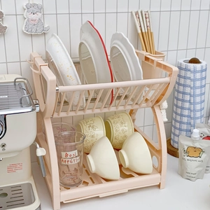 Dual-tier pink kitchen dish drying rack with utensil holder on a white tile background