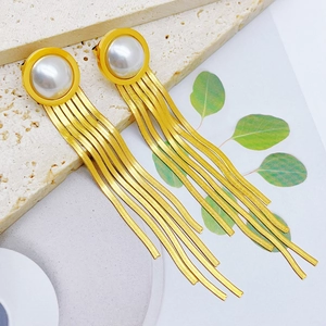 Detail of gold tassel earrings with pearls on a textured stone surface with leaf shadows