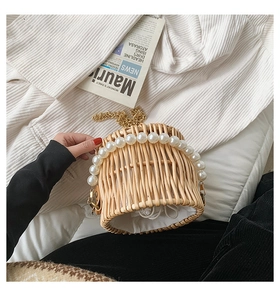 Detail of hand-woven rattan bucket bag featuring large pearl handle and gold chain strap