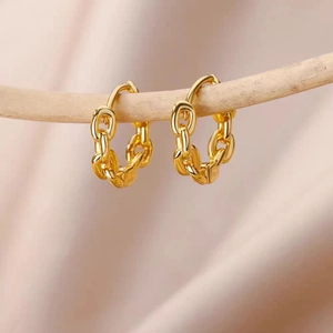 Close-up of gold chunky curb chain hoop earrings hanging on a natural wooden branch
