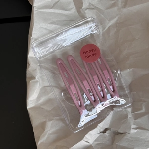 Detail view of 4-piece pink metal hair clips in transparent packaging on brown paper