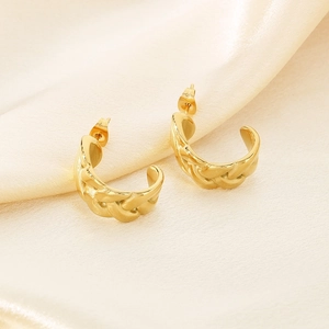 Vue macro de boucles d'oreilles en C dorées avec texture torsadée sur tissu en soie crème