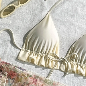 Flat lay of cream halter bikini top with ruffled hem and pink floral print accents
