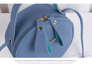 Close-up of blue pebbled leather round bag featuring dual smooth metal zipper closure