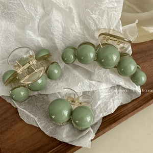 Three sizes of sage green pearl hair claws on a wooden tray with a minimalist design