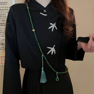 Détail d'un long collier de perles avec pendentif en jade vert et pompon sur haut brodé