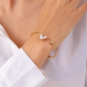 Detail of gold open heart bangle with white shell inlay and crystal on female wrist