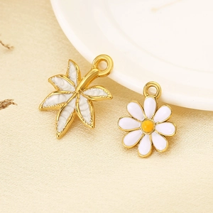 Macro shot of 18K gold plated white enamel daisy and leaf charms for DIY jewelry making