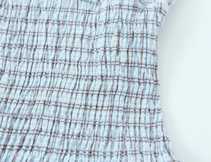 Close-up of light blue and brown plaid fabric with elastic pleated texture detail
