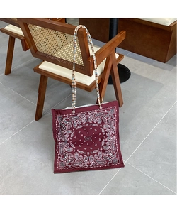 Detail of burgundy paisley tote bag with colorful beaded strap on a wooden chair