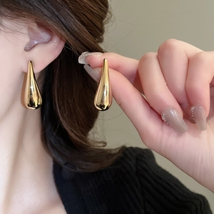 Détail des boucles d'oreilles goutte d'eau en métal doré portées sur l'oreille