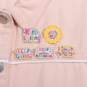 Detail of five enamel pins with motivational quotes pinned on a pink denim collar