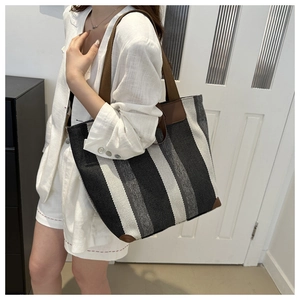 Detail of striped canvas tote bag with reinforced brown leather corners and woven handle
