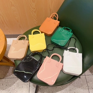Multiple colors of fashionable PVC jelly handbags displayed on a green leather chair