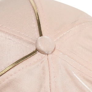 Macro detail of pink satin baseball cap featuring gold metal trim along the seam lines