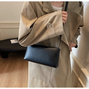 Minimalist black matte leather rectangular crossbody bag with thin strap on a beige coat
