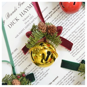 Detail of Christmas bell ornament with green pine needles, pine cones and red velvet bow