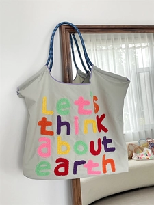 Detail of embroidered earth slogan on grey canvas tote bag with blue woven handles